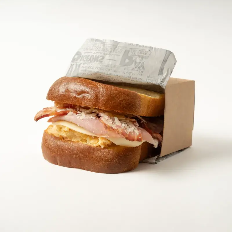 Brioche club con bacon, jamón y queso, en caja de cartón kraft