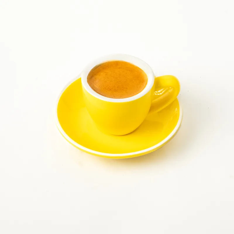 Café espresso con crema en taza pequeña amarilla con platillo