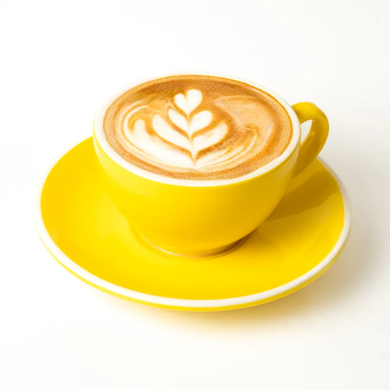 Cappuccino con una hoja dibujada en la espuma, en taza amarilla con platillo