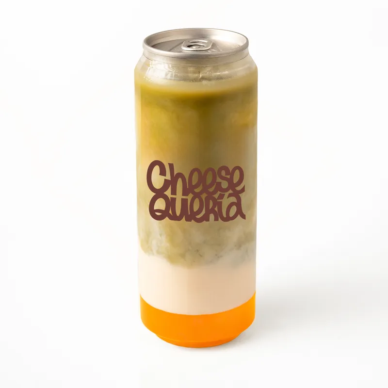 Matcha mango: matcha, leche de avena y mango naranja en el fondo, en lata transparente con el logo de Cheesequería
