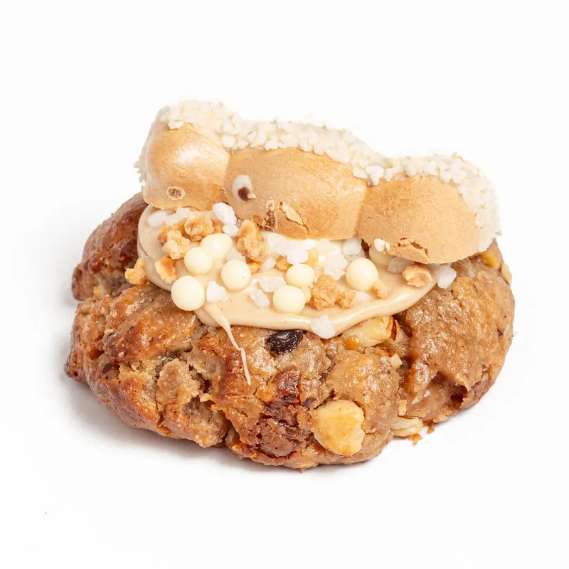 Cookie coronada con una galleta Happy Hippo, crema clara, bolitas blancas y frutos secos picados