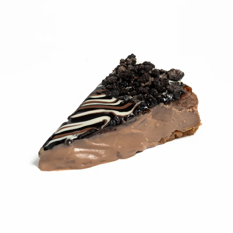 Porción de tarta de queso de chocolate y Oreo con interior de chocolate con leche, galleta triturada e hilos de chocolate